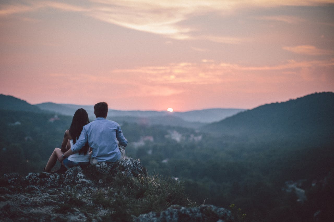 A couple sits on a hill in Budapest, watching the sunset over distant hills, symbolizing love and togetherness.
